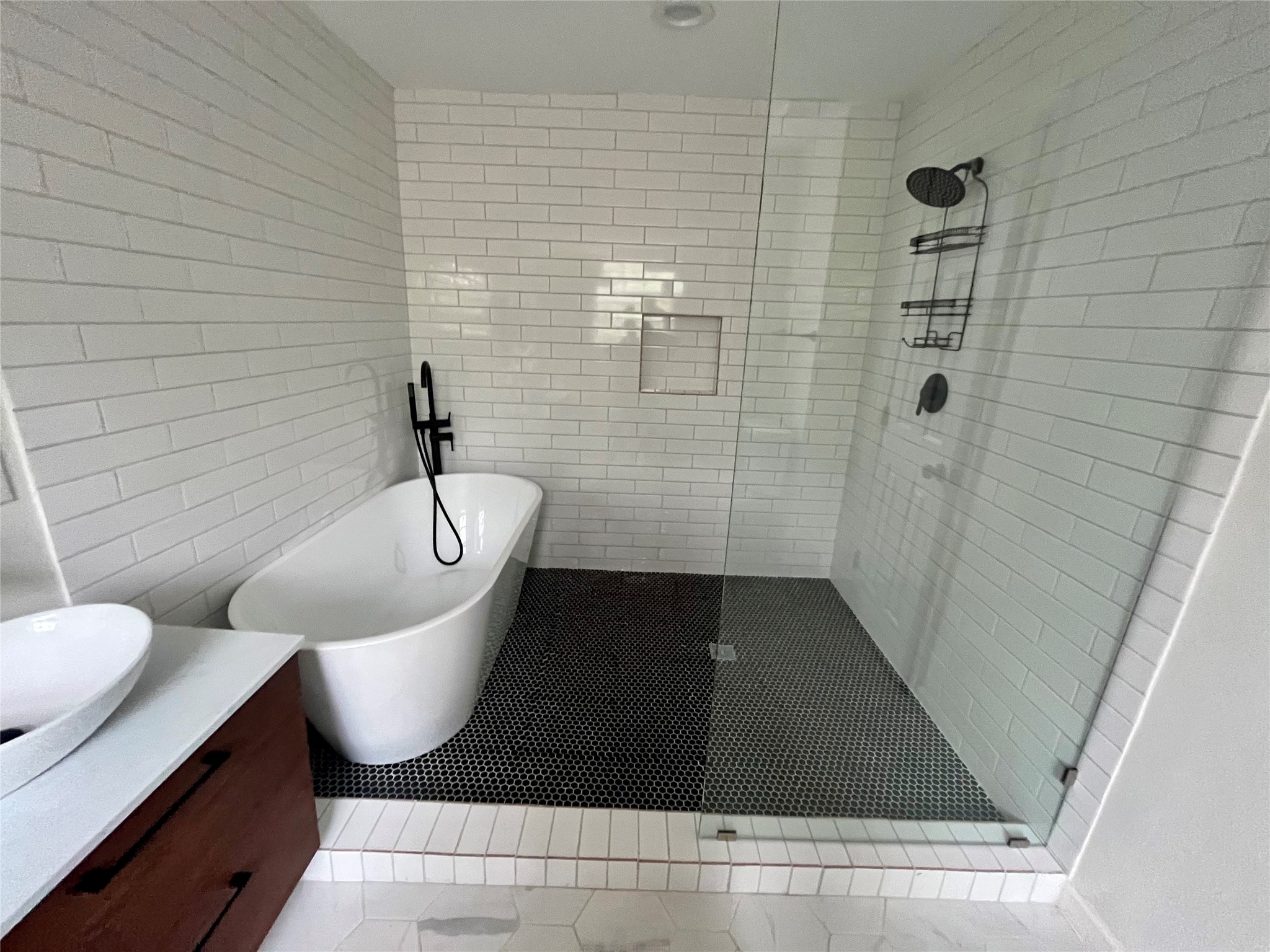 302 Moody Street Houston, TX 77009 - Photo 7 of 11 Stunning bathroom with a freestanding bathtub, glass-enclosed shower, and sleek black fixtures. White subway tiles cover the walls, and a dark hexagonal tile floor adds contrast. The vanity features a vessel sink and wooden cabinetry for a stylish touch.