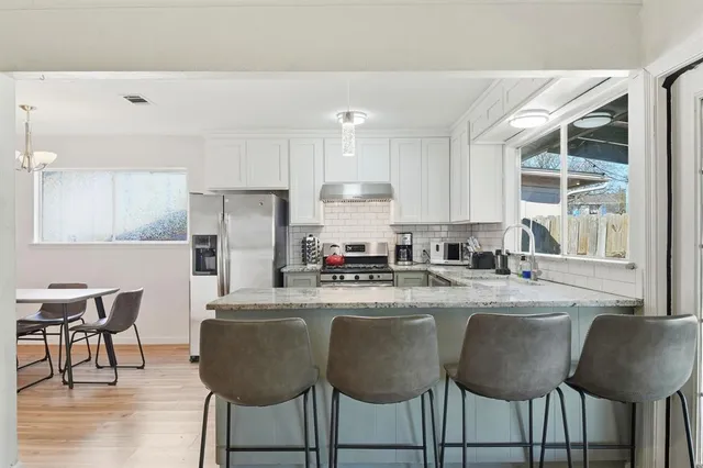 a kitchen with stainless steel appliances granite countertop a dining table chairs refrigerator sink and cabinets