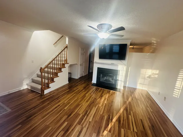 a view of a livingroom with wooden floor a ceiling fan and staircase