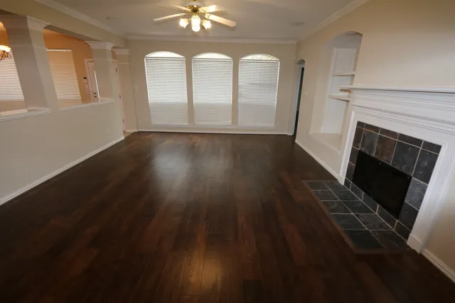an empty room with wooden floor fireplace and windows