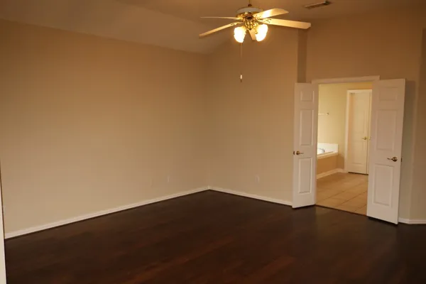 an empty room with a fan and a kitchen view