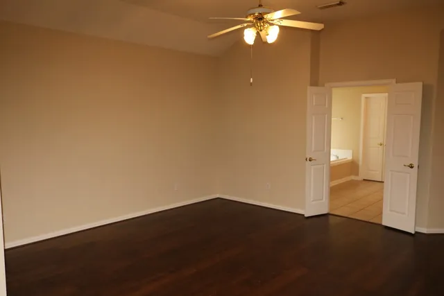 an empty room with a fan and a kitchen view