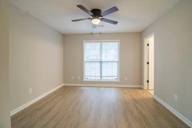an empty room with wooden floor chandelier fan and windows
