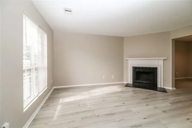 a view of an empty room with wooden floor fireplace and a window
