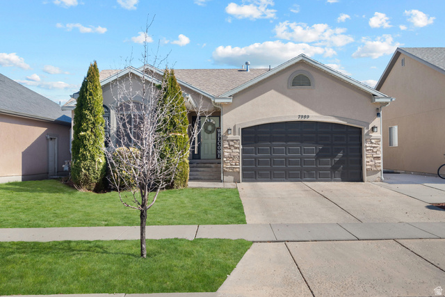 Single story home with a garage, stone siding, driveway, and a front yard