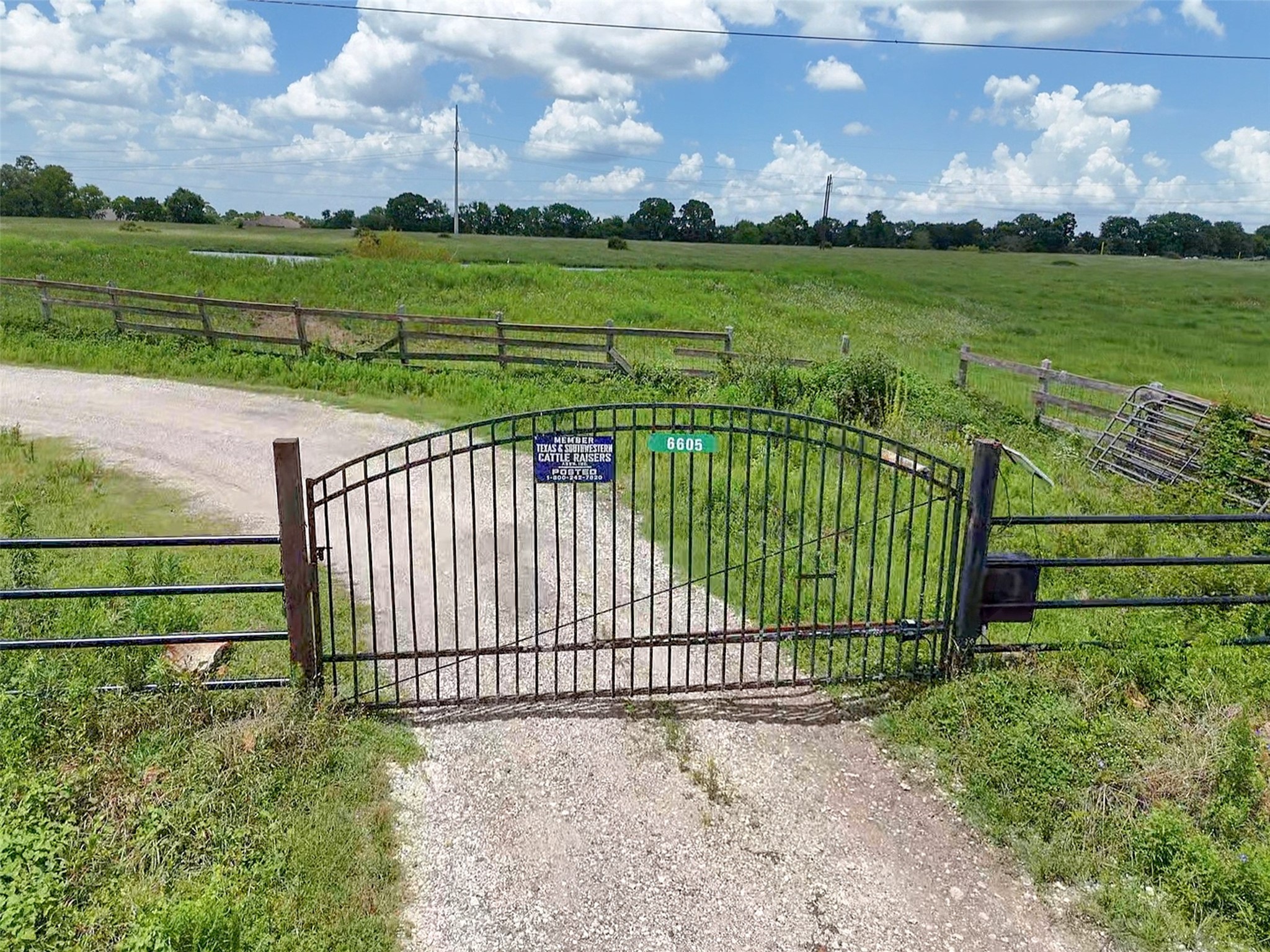 6605 Spring Branch Road Montgomery, TX 77316 - Photo 5 of 12 Welcomed to the property through a custom iron gate that opens to sprawling green pastures and a tree-lined horizon. A peaceful rural retreat awaits just beyond this secure entry.