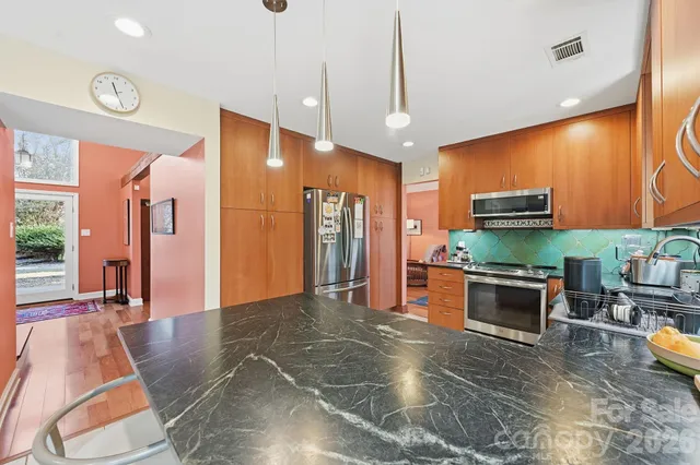 a kitchen with stainless steel appliances kitchen island granite countertop a refrigerator a stove and a sink with wooden floor