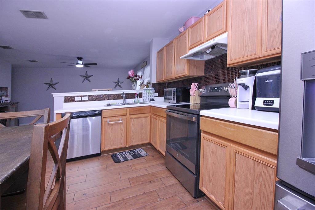 12609 Carpenter Lane Rhome, TX 76078 - Photo 19 of 29 Kitchen featuring wood-finish flooring, light wood cabinetry, stainless steel appliances, and solid surface countertops