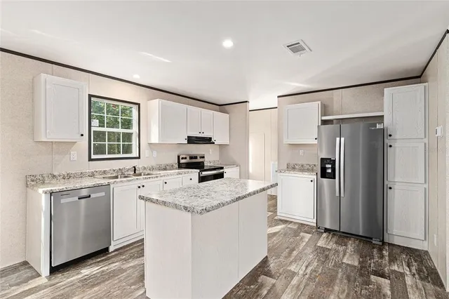 a kitchen with a stove a sink dishwasher a refrigerator and white cabinets with wooden floor