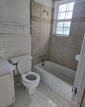 a white toilet sitting next to a bath tub and a window
