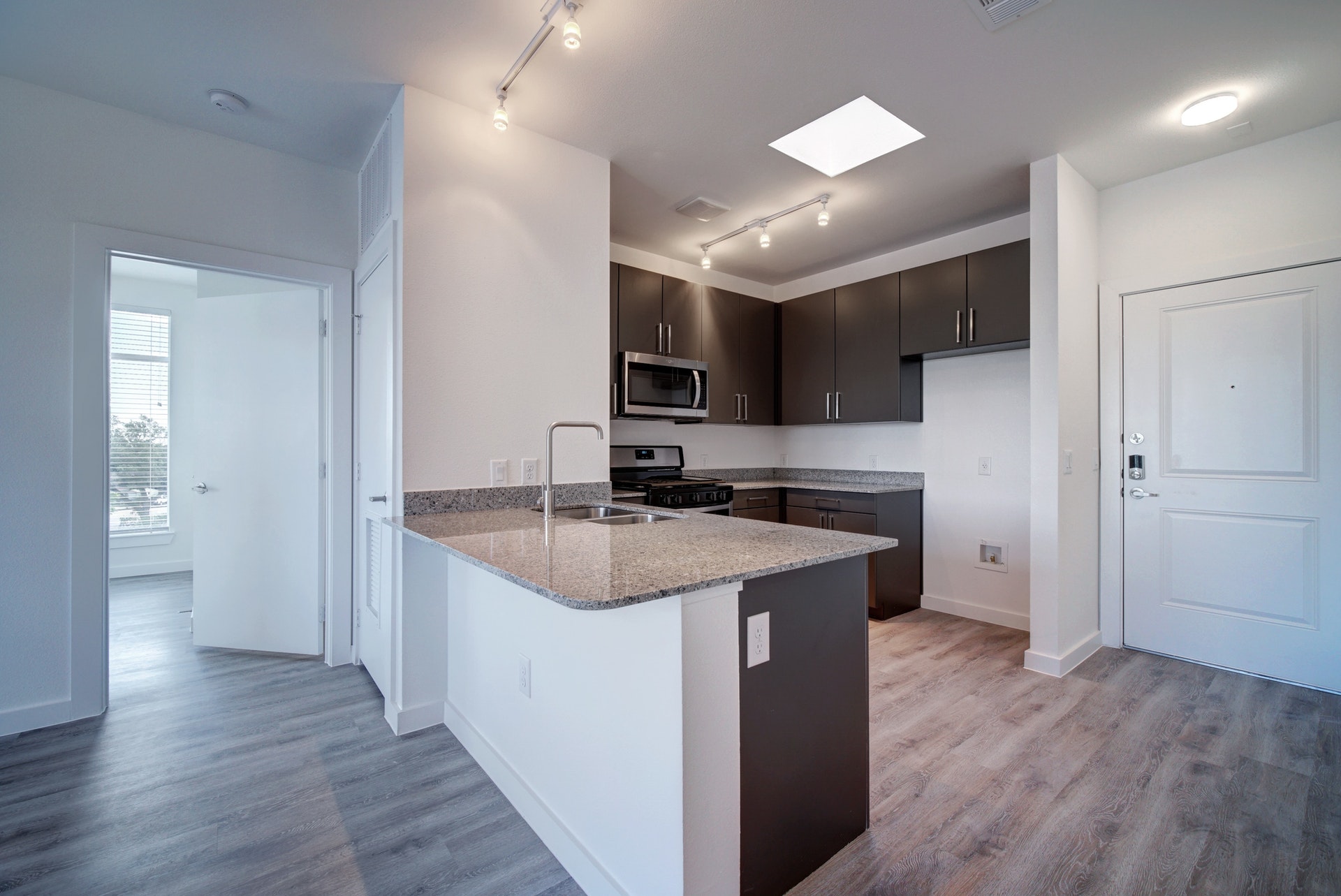 13130 Pond Springs Road, Unit 2203 Austin, TX 78729 - Photo 10 of 32 Kitchen featuring light stone counters, a peninsula, stainless steel appliances, light wood-type flooring, and rail lighting