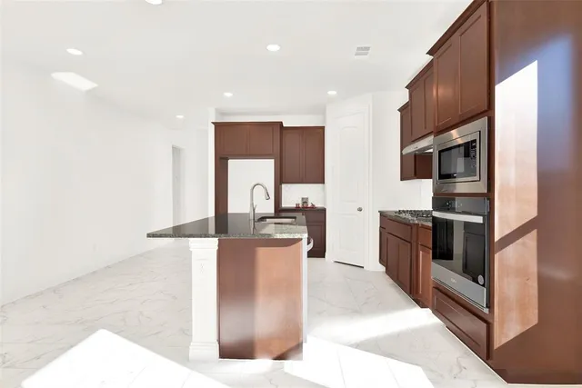 a kitchen with stainless steel appliances kitchen island granite countertop a refrigerator a stove and a sink with wooden floor