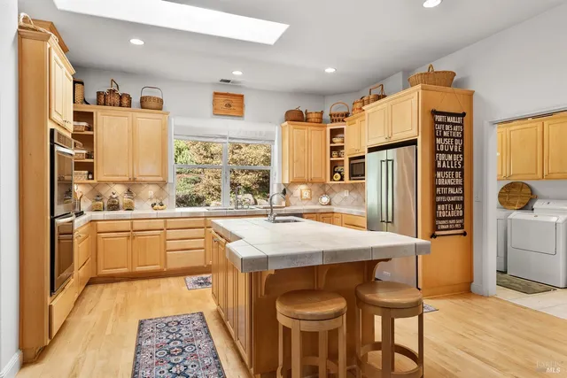 a kitchen with stainless steel appliances kitchen island granite countertop a refrigerator a stove and white cabinets with wooden floor