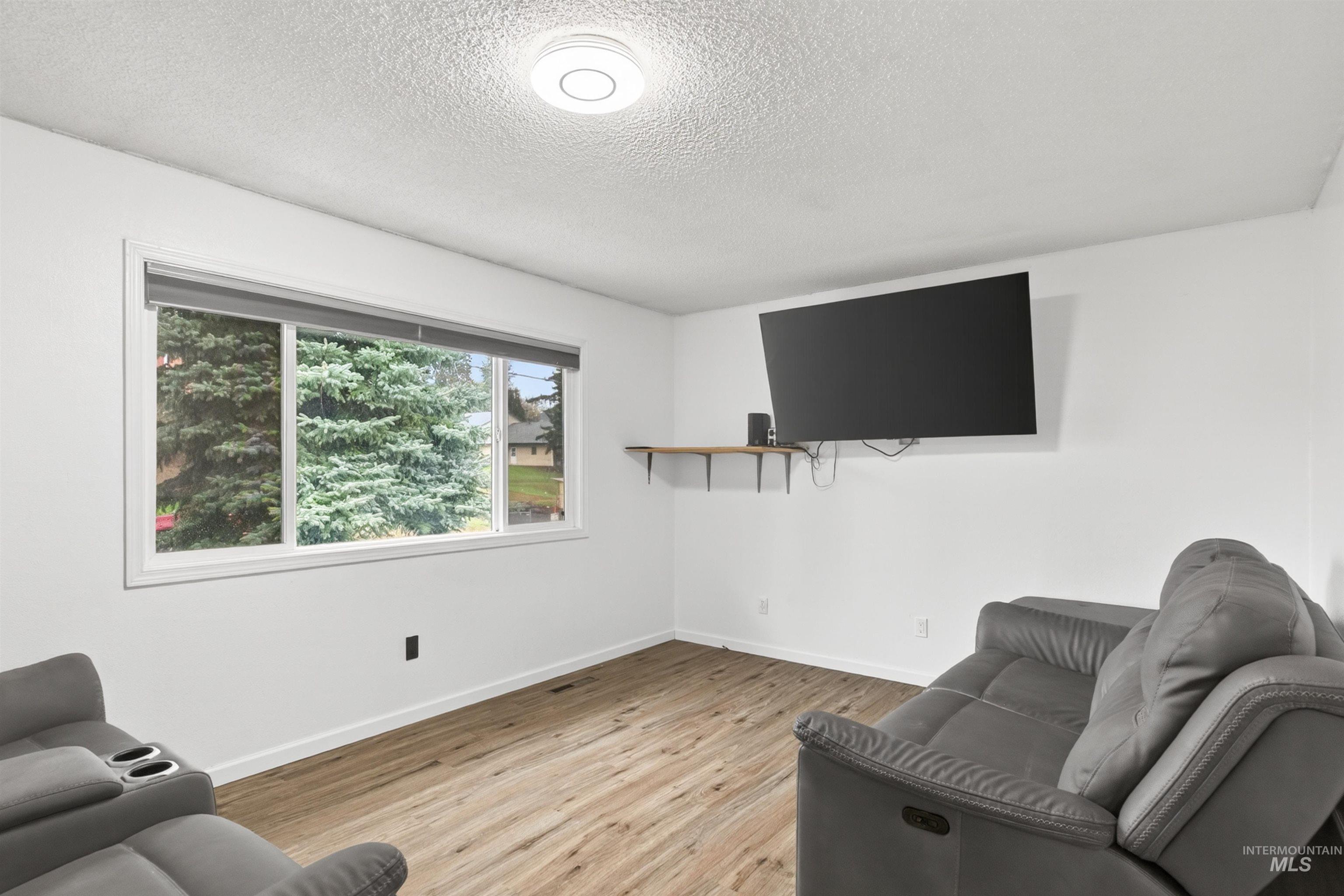 247 North Beech Street Genesee, ID 83832 - Photo 12 of 27 Room featuring a multi-pane window, wood-finish flooring, a wall-mounted television, a floating wall shelf, and a flush-mount ceiling light