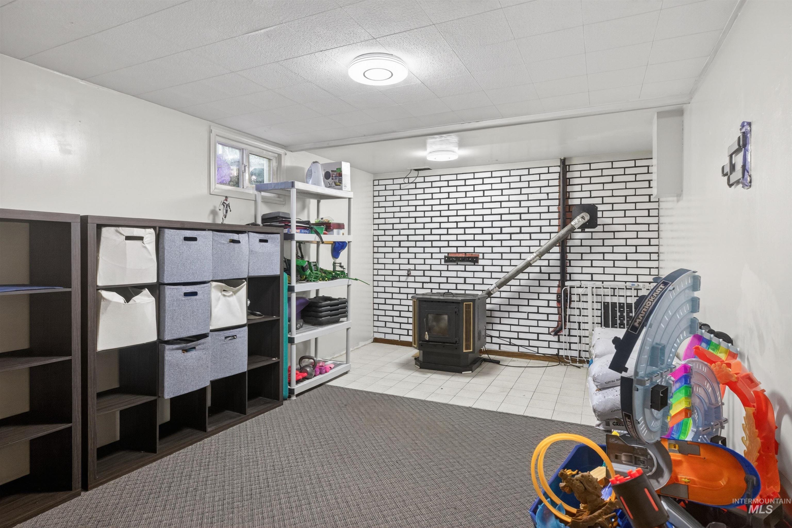 247 North Beech Street Genesee, ID 83832 - Photo 23 of 27 Finished basement area featuring a wood-burning stove with a white brick surround, carpeted flooring, and a drop ceiling