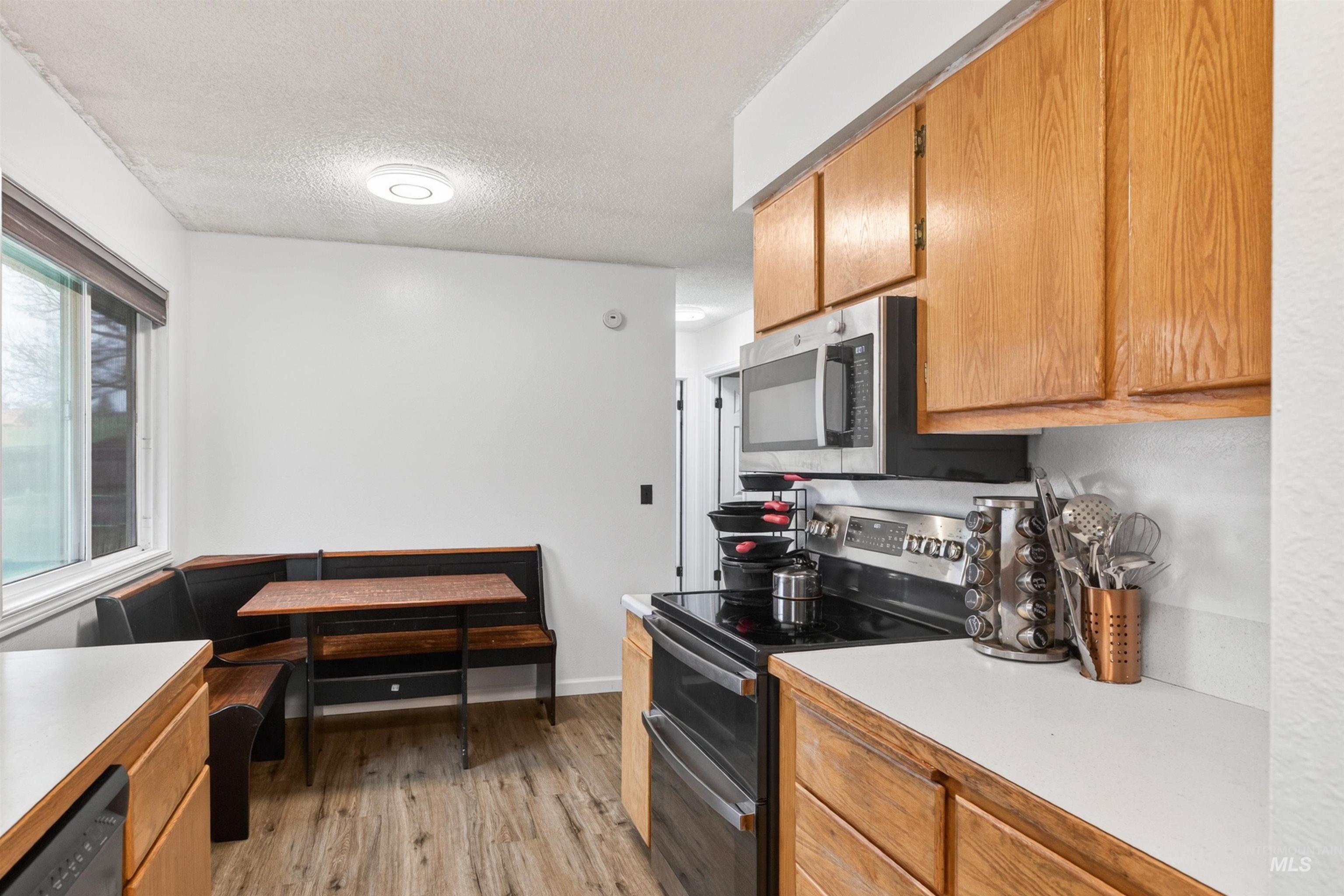 247 North Beech Street Genesee, ID 83832 - Photo 9 of 27 Kitchen featuring a built-in banquette, wood-finish flooring, light wood cabinetry, white countertops, and a full suite of stainless steel appliances including a microwave and range