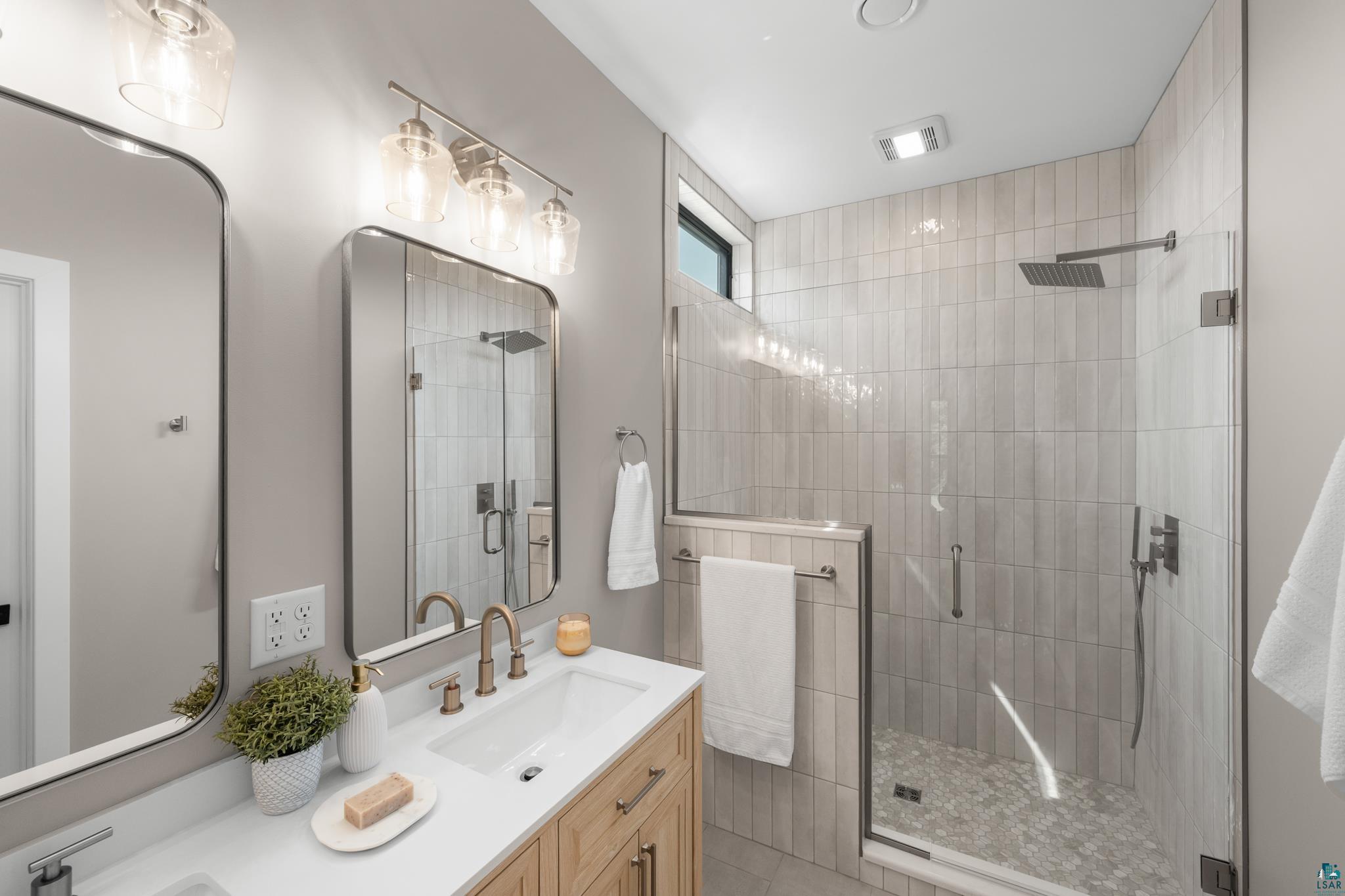 1241 Airport Road Two Harbors, MN 55616 - Photo 38 of 54 Floating wood vanity with a white countertop and rectangular undermount sink, brushed gold faucet, and two framed mirrors