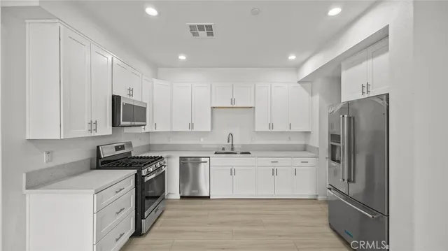 a kitchen with stainless steel appliances granite countertop a stove top oven a refrigerator a sink and dishwasher with white cabinets