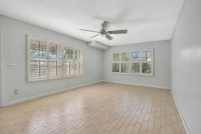 an empty room with wooden floor ceiling fan and windows