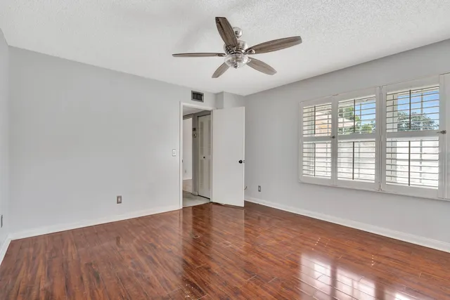 an empty room with wooden floor fan and windows