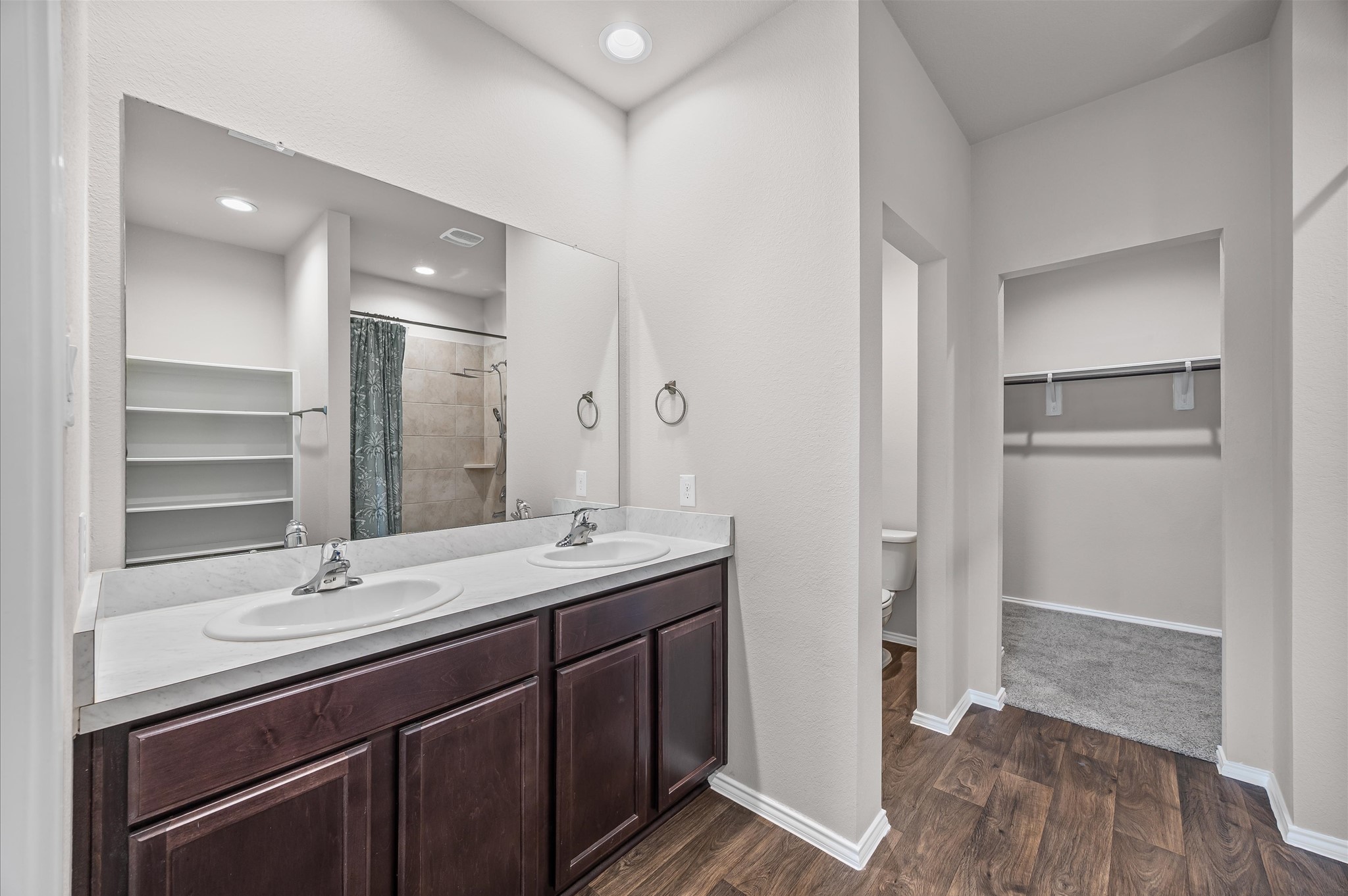 23522 Wedgewood Cliff Way Spring, TX 77373 - Photo 14 of 30 This elegant bathroom boasts a double vanity with rich dark wood cabinets, a spacious mirror, and a walk-in closet. Enhanced by recessed lighting and stylish wood-look flooring, it also features a glimpse of a modern shower area.