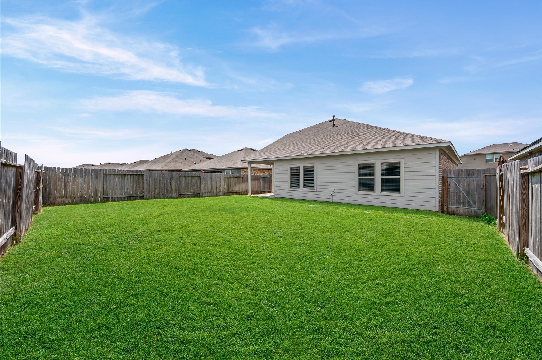 23522 Wedgewood Cliff Way Spring, TX 77373 - Photo 28 of 30 Spacious backyard with lush green grass, surrounded by a wooden fence. Perfect for outdoor activities and privacy. The house features a simple, modern exterior with multiple windows.