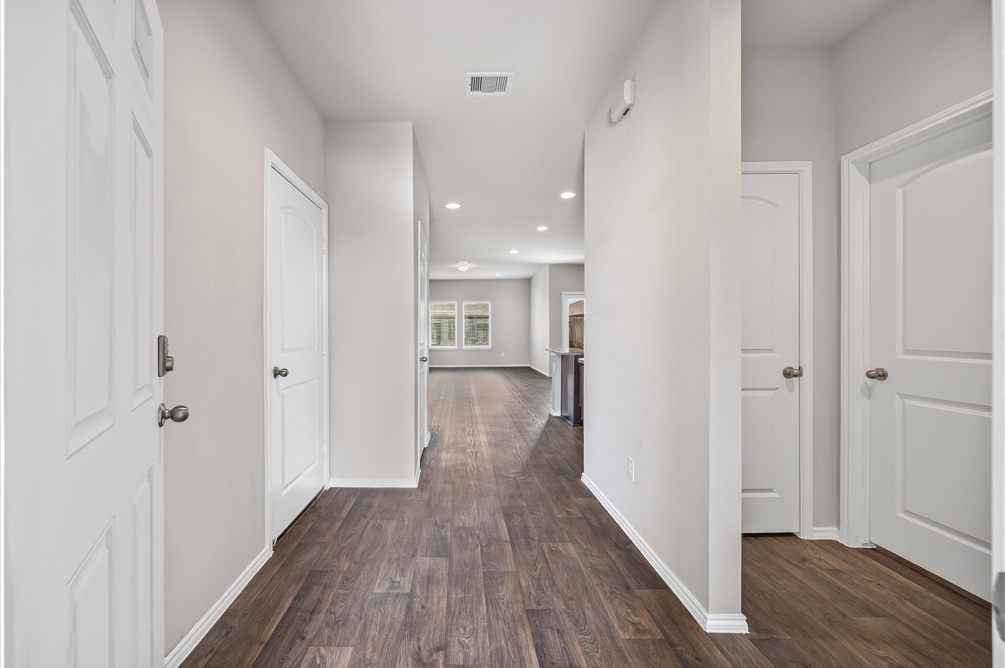 23522 Wedgewood Cliff Way Spring, TX 77373 - Photo 4 of 30 A bright, long hallway with wood look vinyl flooring and freshly painted walls, lead to an open living area. There are multiple doors to explore along the sides, and recessed lighting adds a modern touch.