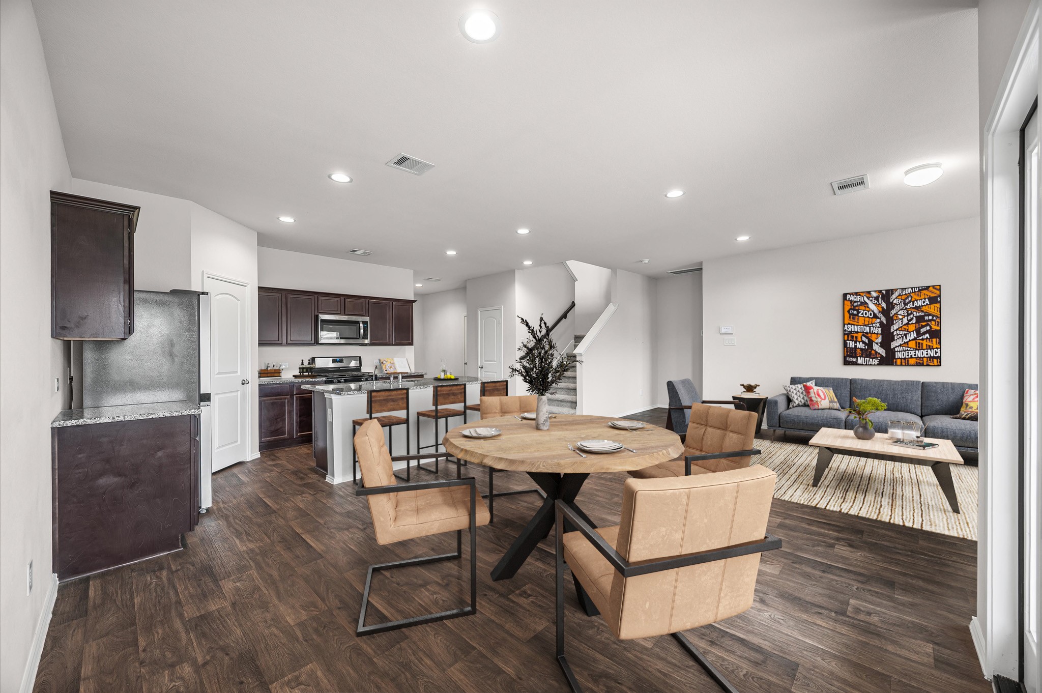 23522 Wedgewood Cliff Way Spring, TX 77373 - Photo 7 of 30 *Virtually Staged*This open-concept living space features a modern kitchen with dark cabinets and stainless steel appliances, seamlessly flowing into a dining area with a round table. The adjacent living area includes a staircase leading upstairs. The space is well-lit with recessed lighting and has warm flooring throughout.