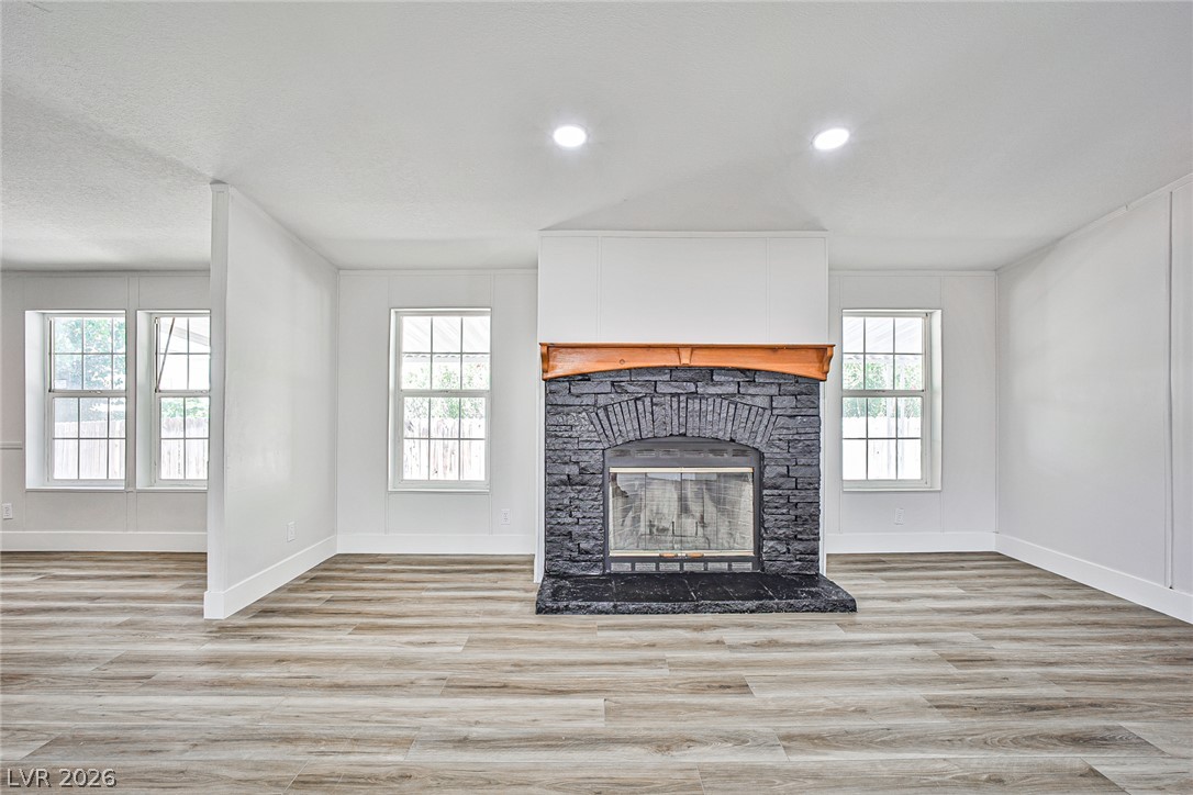 273 Aztec Lane Henderson, NV 89015 - Photo 11 of 28 A spacious room features a dark stone fireplace with a rustic wood mantle, complementing the light wood-look flooring.