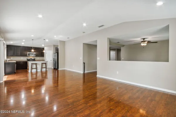 a view of empty room with kitchen view and wooden floor