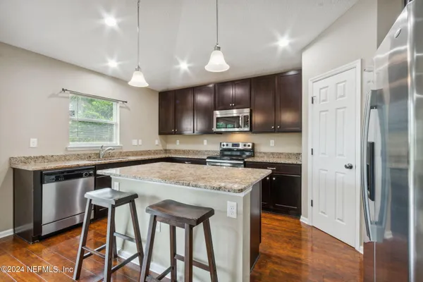 a kitchen with stainless steel appliances granite countertop a stove top oven a refrigerator a sink and a dining table with white cabinets