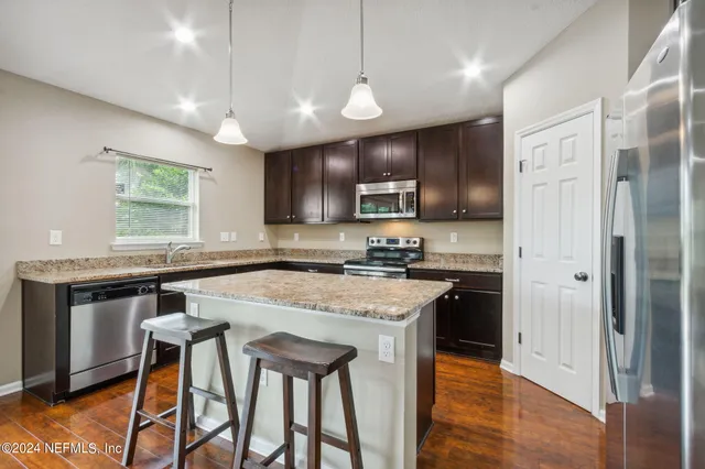 a kitchen with stainless steel appliances granite countertop a stove top oven a refrigerator a sink and a dining table with white cabinets