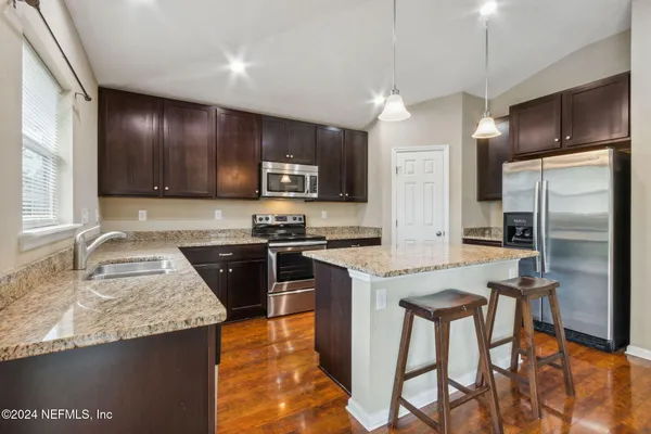 a kitchen with stainless steel appliances granite countertop wooden cabinets a refrigerator a stove a sink and a oven with wooden floor