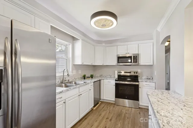 a kitchen with stainless steel appliances granite countertop a refrigerator a stove top oven a sink and dishwasher with wooden floor