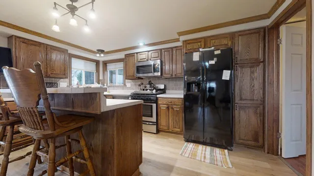 a kitchen with stainless steel appliances granite countertop a refrigerator a sink dishwasher a stove and a dining table with wooden floor