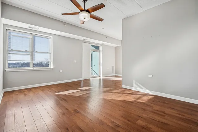 an empty room with wooden floor fan and windows