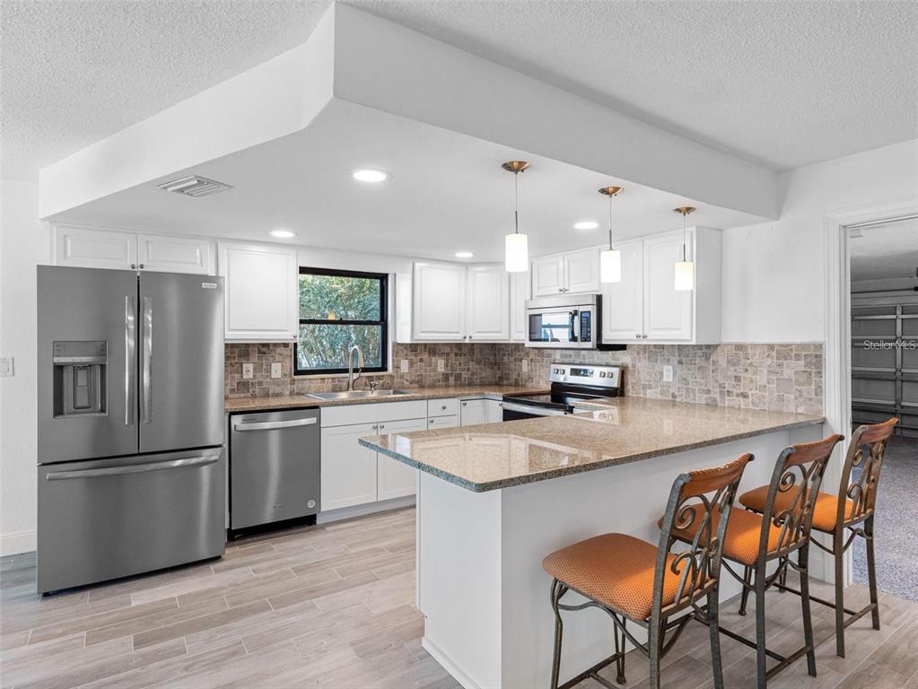 562 Johns Pass Avenue Madeira Beach, FL 33708 - Photo 27 of 51 a kitchen with stainless steel appliances granite countertop a table chairs sink refrigerator and cabinets