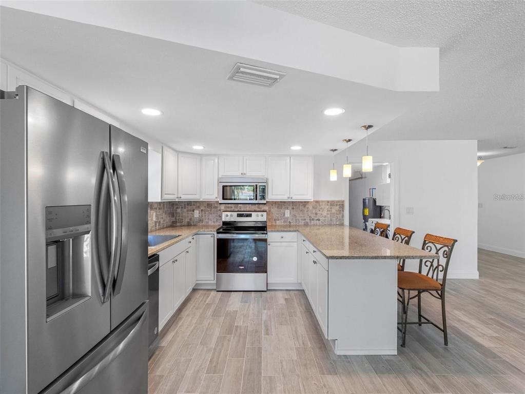 562 Johns Pass Avenue Madeira Beach, FL 33708 - Photo 28 of 51 a kitchen with stainless steel appliances granite countertop a refrigerator a stove top oven a sink dishwasher with a dining table and chairs