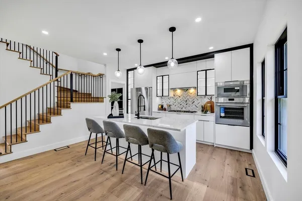 a kitchen with stainless steel appliances kitchen island granite countertop a refrigerator a stove a sink and white cabinets with wooden floor