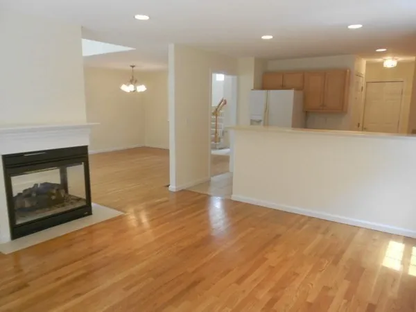 a view of an empty room and kitchen with fireplace wooden floor