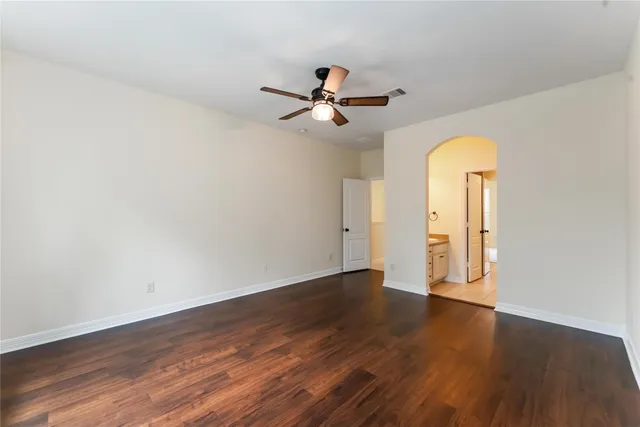 an empty room with wooden floor chandelier fan and windows