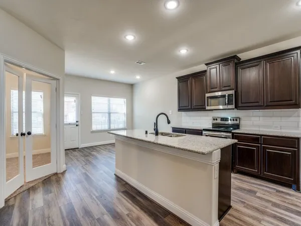 a kitchen with stainless steel appliances granite countertop wooden cabinets a sink a stove a refrigerator and dishwasher with wooden floor