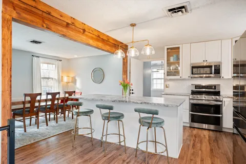 a kitchen with stainless steel appliances granite countertop a stove top oven a sink a dining table and chairs with wooden floor