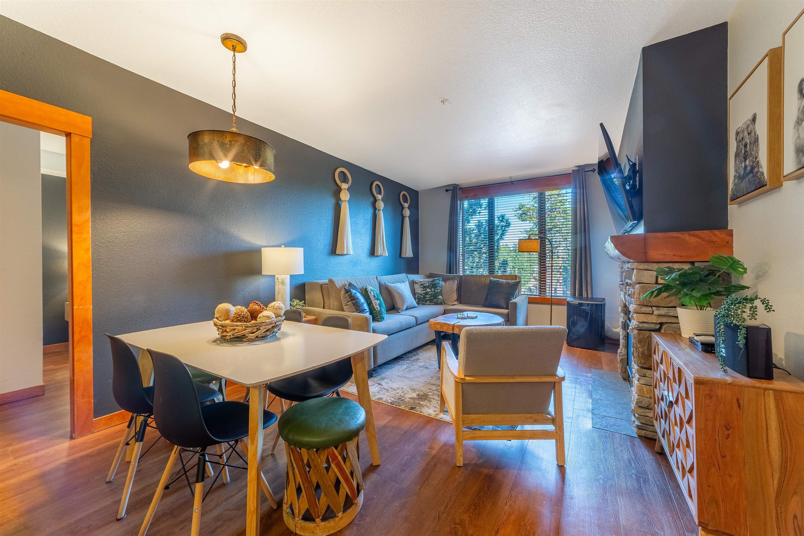 6201 Minaret Road, Unit 2221 Mammoth Lakes, CA 93546 - Photo 10 of 44 Open-concept living area featuring wood-finish flooring, a stone-clad fireplace with a wood mantle, a dining area with pendant lighting, and abundant natural light from large windows