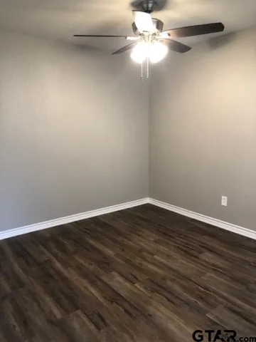a view of an empty room with wooden floor and a chandelier fan