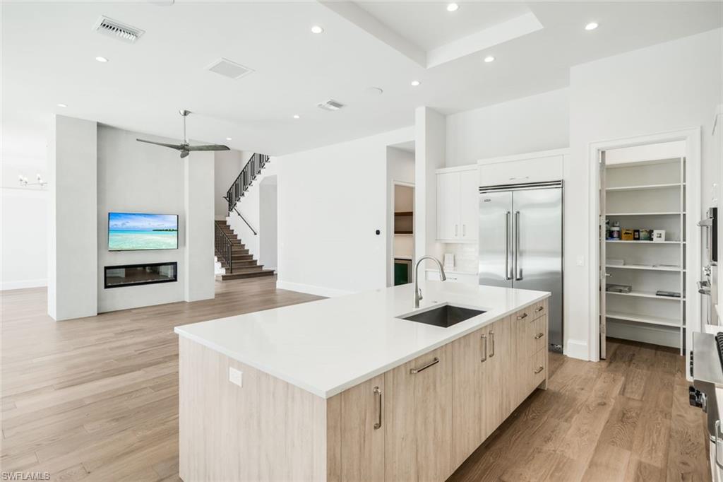 16716 Enclave Circle Naples, FL 34110 - Photo 13 of 50 Two tone kitchen with a kitchen island with sink, light wood-type flooring, stainless steel appliances, modern cabinets, and recessed lighting