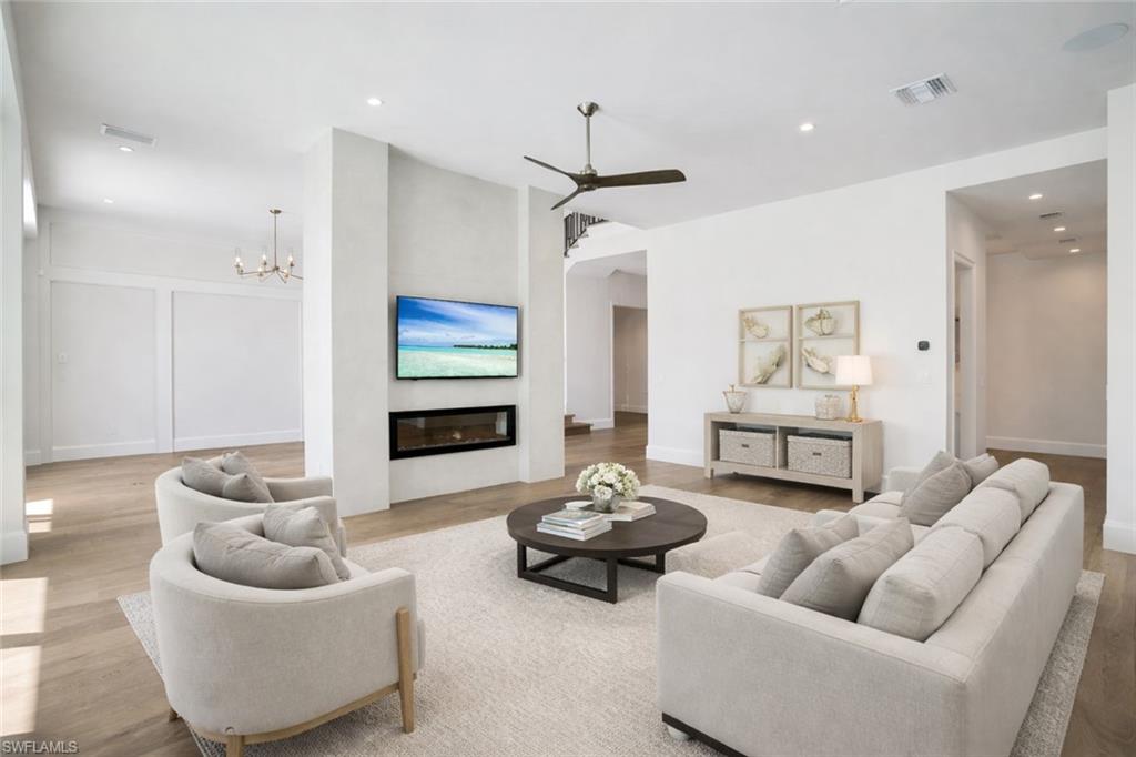 16716 Enclave Circle Naples, FL 34110 - Photo 14 of 50 Living area with a glass covered fireplace, light wood-style floors, ceiling fan, and a chandelier