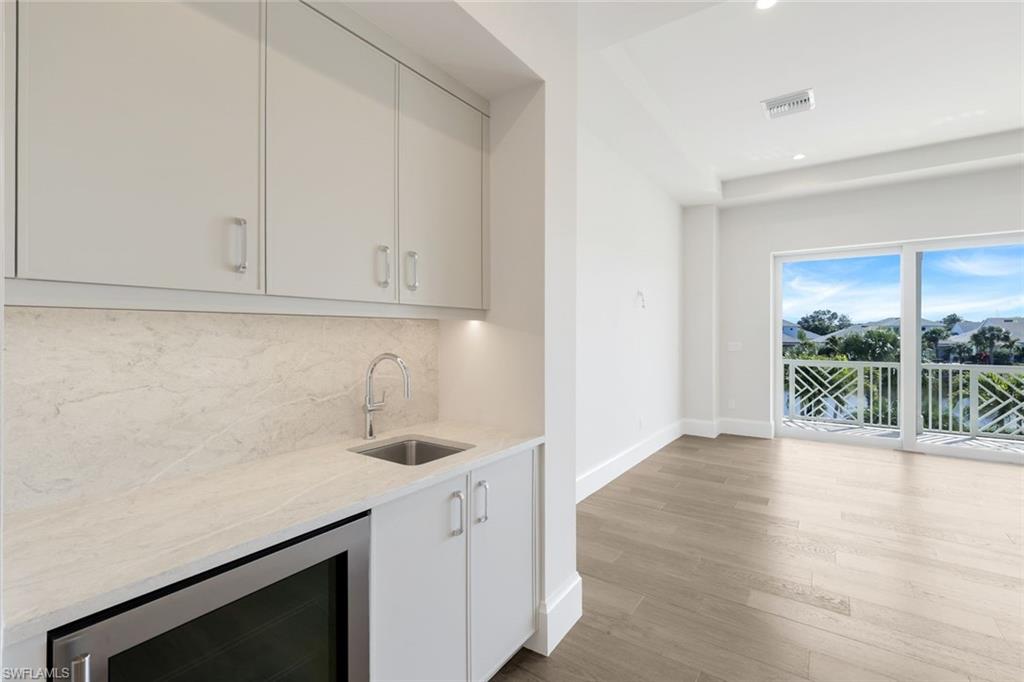 16716 Enclave Circle Naples, FL 34110 - Photo 25 of 50 Indoor wet bar with beverage cooler, light stone counters, light wood-type flooring, recessed lighting, and tasteful backsplash