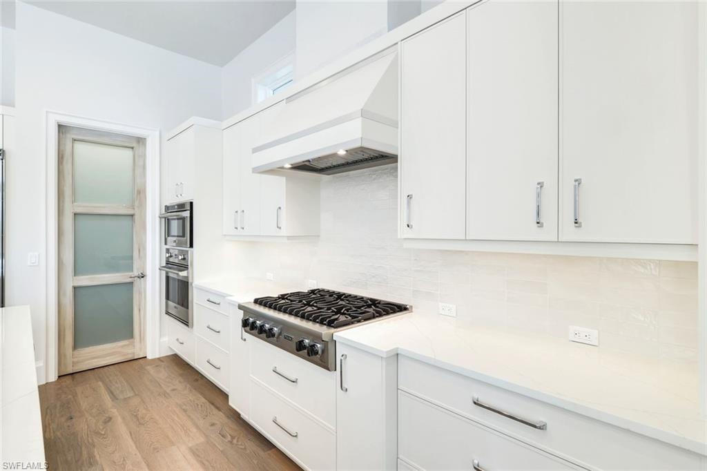 16716 Enclave Circle Naples, FL 34110 - Photo 9 of 50 Kitchen featuring white cabinetry, stainless steel appliances, light wood-style floors, and decorative backsplash