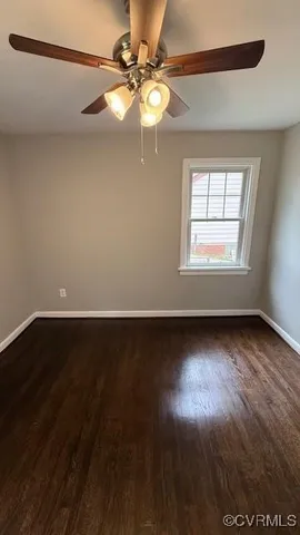 a view of an empty room with wooden floor and fan